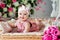 Small very cute wide-eyed smiling baby girl in a pink dress lying in a wicker basket about pink tulips
