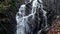 Small waterfall full of water after rain. Reflections on wet basalt boulders, milky water full of streams and bubbles..