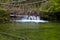 A small waterfall with green water and fallen trees in the Slovak Paradise National Park