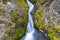 A small waterfall in the mountains between two moss-covered cliffs