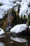 Small waterfall and pond in a winter landscape, snow covered rocks and bushes, reflections