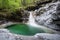 A small waterfall runs over white rock and into an emeral pool