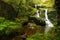 Small waterfalls falling on mossy rocks near a stone water-mill