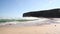 Small waves on a tropical beach breaking on sand, blue sky and a cliff in the background