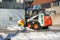 A small wheel loader removes snow on the city sidewalk