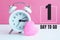 A small white alarm clock and a pink heart figurine. The inscription`1 day to go