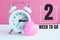 A small white alarm clock and a pink heart figurine. The inscription`2 week to go