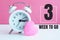 A small white alarm clock and a pink heart figurine. The inscription`3 week to go