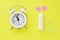 small white alarm clock, pink hearts and a tampon against a yellow background. space for text