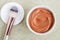 Small white bowl with red cosmetic clay mask. Homemade beauty treatment. Copy space