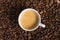 Small white coffee cup with espresso crema on roasted beans background. Selective focus