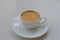 Small white cup with aromatic light brown coffee on a saucer