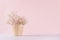 Small white dried flowers in beige wicker basket on soft pink pastel background. Fresh light gentle background.