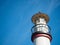 A small white lighthouse with an iron roof on the right against a blue sky