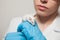 A small white mouse with red eyes in the hand of a scientist in a blue rubber glove.