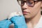 A small white mouse with red eyes in the hand of a scientist in a blue rubber glove.