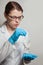 A small white mouse with red eyes in the hand of a scientist in a blue rubber glove.