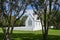Small white traditional design chapel surrounded by white picket fence viewed between pohutukawa trees