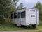 Small white trailer house with blue sign office, abandoned caravan in rural landscape near footpath, green grass and trees