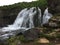 A small wide waterfall cascades onto rocks in Iceland.