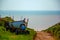 A small wooden boat is left on a towing wagon by a dirt path near the ocean