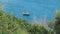 Small wooden boat rocking on the waves. Bay is surrounded by greenery. Blue Sea has a slight wave.