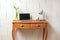 Small wooden console table with laptop, desk lamp and a piggy bank as a place for a tiny home office against a bare white wall,