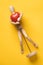 Small wooden figurine gently hugs a red tomato in the form of a heart, a symbol of love, lying on a yellow background