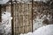 Small wooden plank entrance gate in winter with wire fence