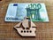 A small wooden or plywood flat toy ship and Euro banknotes next to it. The concept of the value of the toy, travel, and