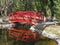 Small wooden red bridge in a park with its reflection on a placid river below