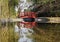 Small wooden red bridge in a woodland with its reflection on a placid river below