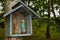 A small wooden shrine hanging on a birch tree, near other trees.