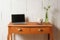 Small wooden vintage table with laptop, piggy bank and flower vase against a rough white wall, tiny home office, copy space