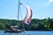 Small yacht with a colorful sail in the front cruising through a lake on a sunny summerday with a forest in the background