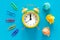Small yellow alarm clock on blue background, Colorful office staples and crumpled paper balls. Top View. The concept of office wor