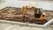 a small yellow excavator levels the ground on a playground for mounting a swing