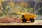 A small yellow toy truck is loaded with brown grains of buckwheat around a buckwheat pile. A car on a wooden surface against a ba