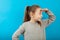 Small young beautiful girl search and looking far away with hand over head. Portrait on blue background