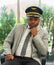 Smart african man in airline sitting, wearing pilot hat and looking to camera in meeting room