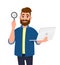 Smart bearded young man showing/holding magnifying glass and laptop computer in hand. Search, find, discovery, analyze, inspect.