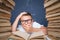 Smart boy in glasses getting crazy of reading book while sitting between two piles of books