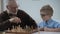 Smart child playing chess with grandfather, family having fun, early development