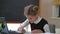 Smart confident teenage schoolgirl watching online lesson writing with pen sitting at desk indoors. Portrait of