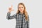 Smart cute little girl raising one finger up, looking thoughtful and clever, standing over white background in casual shirt