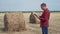Smart farming agriculture concept. Man farmer worker studying a haystack in a field on digital tablet. Slow motion video