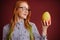 Smart ginger young woman in glasses holding mango on red background