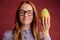 Smart ginger young woman in glasses holding mango on red background