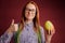 Smart ginger young woman in glasses holding mango on red background