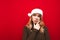 Smart girl in santa hat and warm sweater isolated on red background, looks away at copy space and thinks close portrait. Pensive